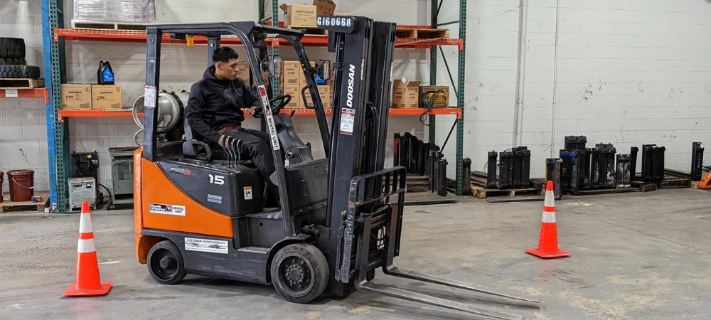 student training on forklift inside warehouse navigating between orange cones